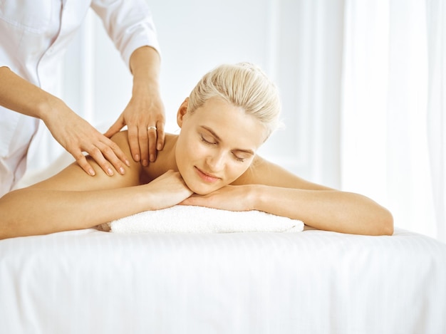 Mooie blonde vrouw genieten van rugmassage met gesloten ogen. Spa salon concept.