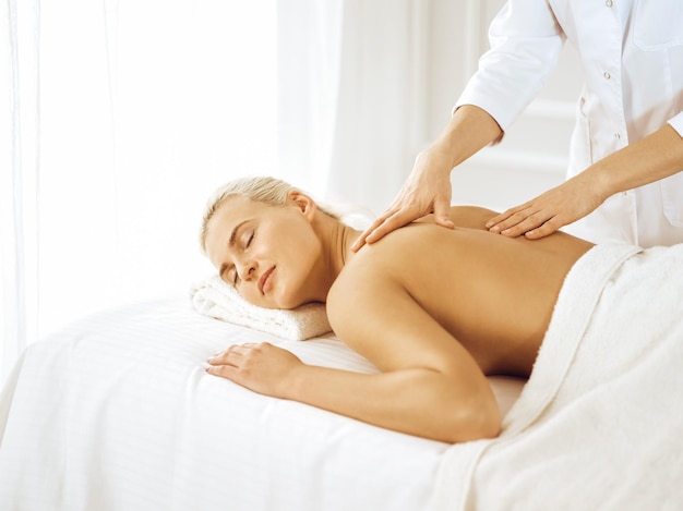 Mooie blonde vrouw genieten van rugmassage met gesloten ogen. Spa salon concept.