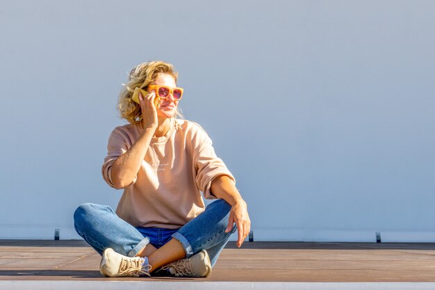 Mooie blonde vrouw in casual kleding zitten en praten aan de telefoon. Mensen levensstijl concept. Kopieer ruimte voor kopiëren.