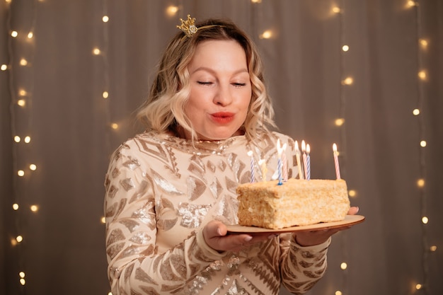 Mooie blonde vrouw in een kleine kroon op haar hoofd met een verjaardagstaart en kaarsen.