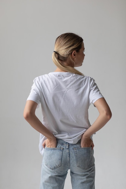 Mooie blonde vrouw in een wit T-shirt en blauwe spijkerbroek die op een witte achtergrond poseert