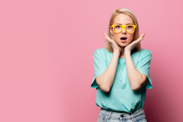 Mooie blonde vrouw in gele bril op roze muur