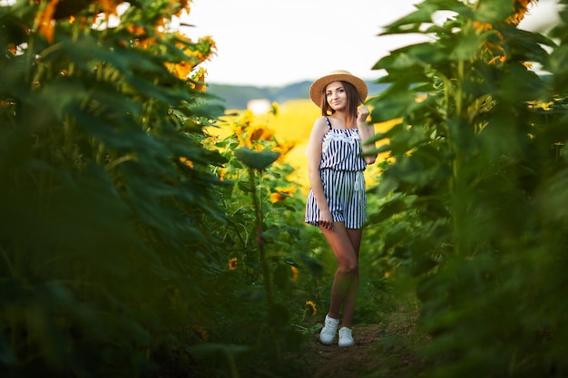 Mooie blonde vrouw in het bloemenveld op zonsondergang in strohoed