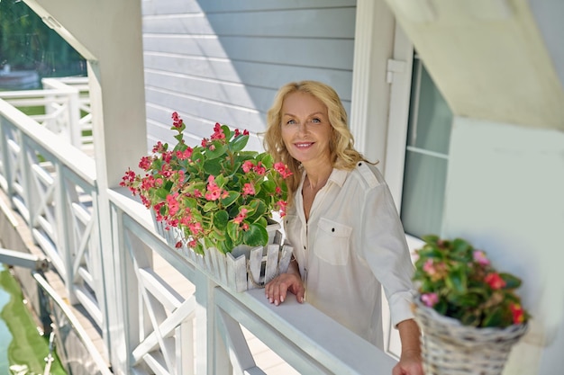 Mooie blonde vrouw in het wit met de bloemen bij haar thuis