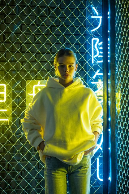 Foto mooie blonde vrouw in witte hoodie en blauwe spijkerbroek die poseert tegen een neon achtergrond