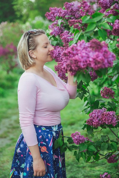 Mooie blonde vrouw inhaleert de geur van seringen in de tuin