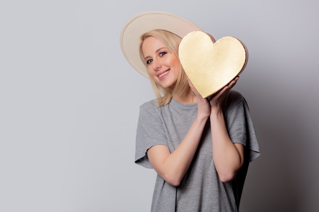 Mooie blonde vrouw met de doos van de hartvorm op witte muur