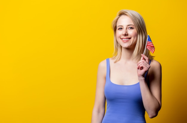 Mooie blonde vrouw met de vlag van de VS op gele muur