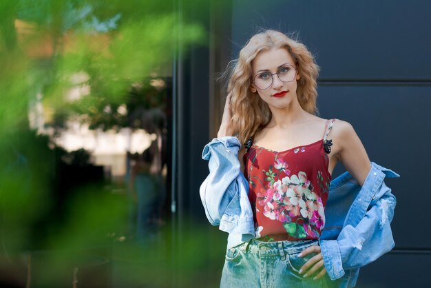 Mooie blonde vrouw met een bril en blauwe denim en spijkerbroek die zich voordeed op straat in de stad