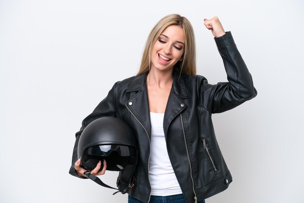 Mooie blonde vrouw met een motorhelm die op witte achtergrond wordt geïsoleerd die een overwinning viert