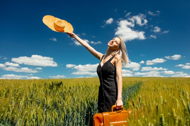 Mooie blonde vrouw met koffer in een tarweveld in zonnige dag