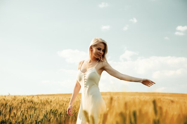 Mooie blonde vrouw op tarwegebied in zonsondergangtijd