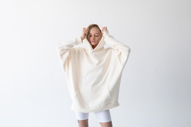 Foto mooie blonde vrouw poseert in een witte hoodie en leggings op een witte achtergrond