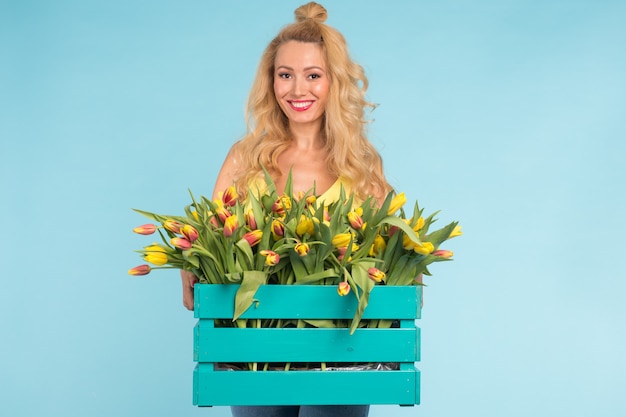 Mooie blonde vrouw tuinman bedrijf doos met tulpen op blauwe achtergrond