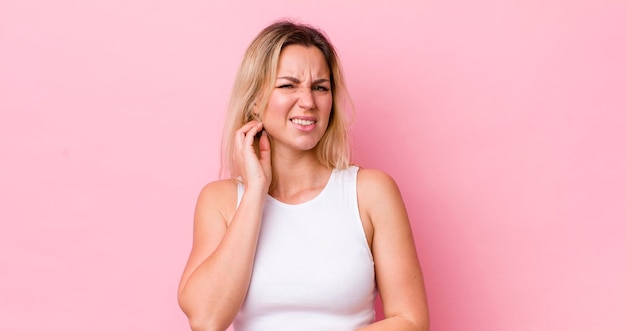 Mooie blonde vrouw voelt zich gestrest, gefrustreerd en moe en wrijft over pijnlijke nek met een bezorgde, verontruste blik