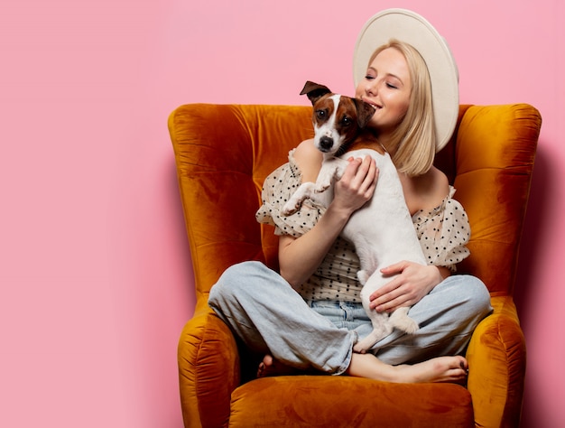 Mooie blonde womanwith een hond in een fauteuil op roze muur