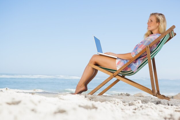 Mooie blonde zittend op strand met haar laptop