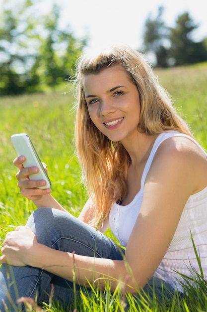 Mooie blonde zitting op gras die een tekst verzenden