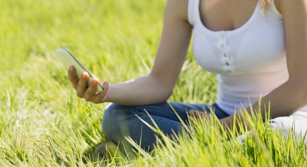 Foto mooie blonde zitting op gras die een tekst verzenden