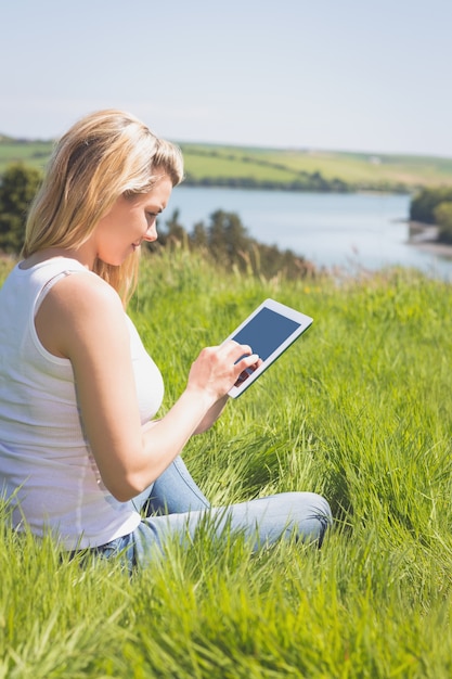 Mooie blonde zitting op gras die haar tablet gebruiken