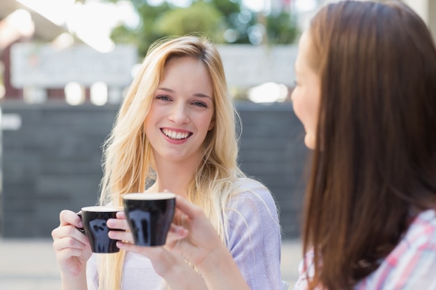 Mooie blondevrouw die bij camera glimlachen en een kop van koffie houden