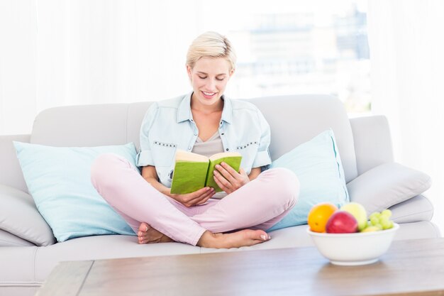 Mooie blondevrouw die een boek op de laag lezen