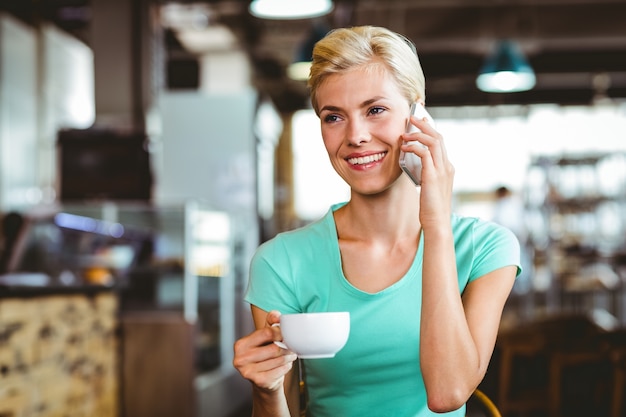 Mooie blondevrouw die haar smartphone met een kop van koffie gebruiken