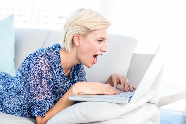 Mooie blondevrouw die op de laag liggen en haar laptop met behulp van