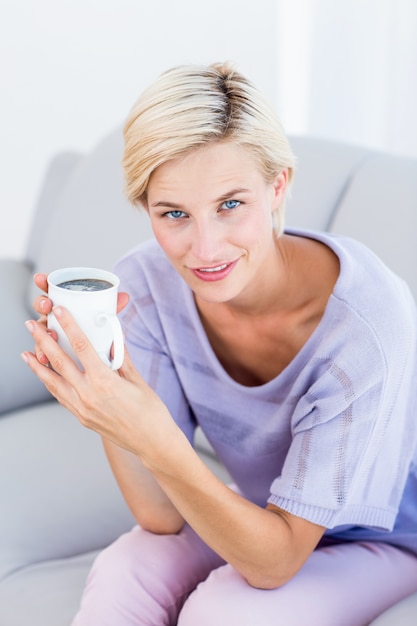 Mooie blondevrouw die op de laag ontspannen en een mok houden