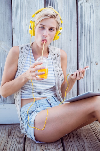 Mooie blondevrouw het luisteren muziek met haar mobiele telefoon en het drinken jus d&#39;orange