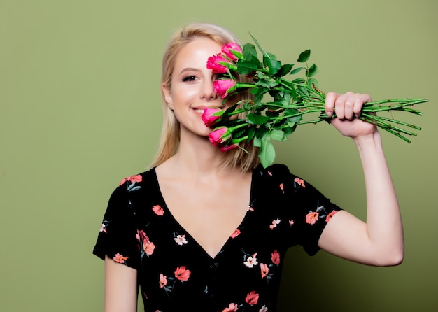 Mooie blondevrouw in kleding met rozen op groene muur