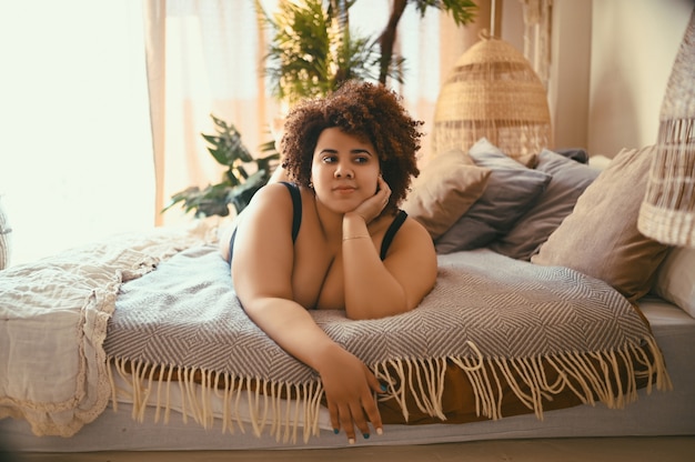 Mooie bochtige oversized Afrikaanse zwarte vrouw afro haar liggend op bed eco vriendelijke slaapkamer gezellig