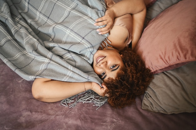 Mooie bochtige plus size Afrikaanse zwarte vrouw afro haar liggend op bed met grijze geruite deken gezellig