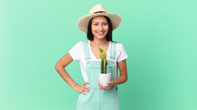 Mooie boerenvrouw die gelukkig lacht met een hand op de heup en zelfverzekerd en een cactus vasthoudt