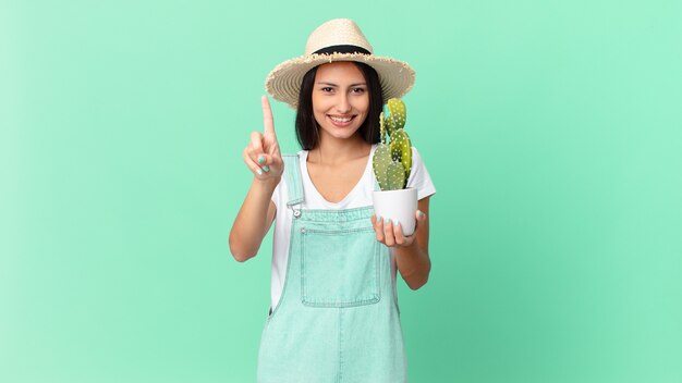 Mooie boerenvrouw die trots en zelfverzekerd glimlacht en nummer één maakt en een cactus vasthoudt