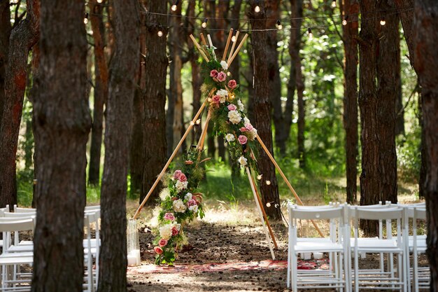 Foto mooie boheemse tipi-boogdecoratie op de buitenlocatie van de huwelijksceremonie in dennenbos met kegels