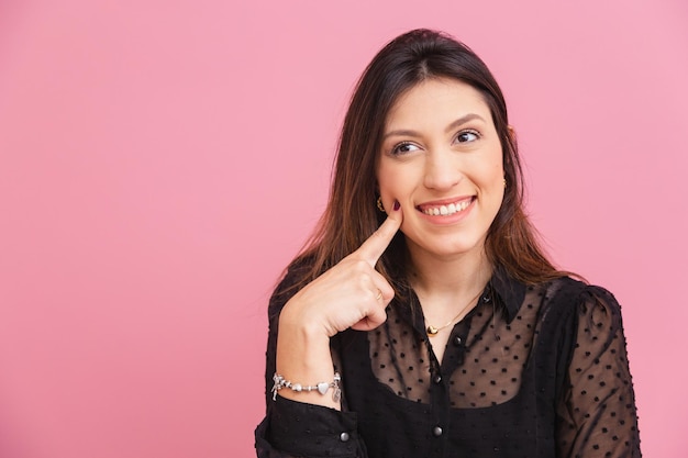 Mooie braziliaanse blanke vrouw roze achtergrond wijzend naar wang en glimlach concept van esthetiek schoonheid uiterlijk