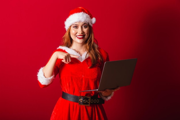 Mooie Braziliaanse roodharige vrouw, gekleed in kerstkleding Santa Claus die een notitieboekje vasthoudt Wauw ongelooflijk ongelooflijk