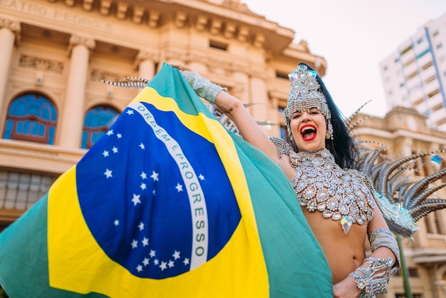 Mooie Braziliaanse vrouw die kleurrijk Carnaval-kostuum en de vlag van Brazilië draagt tijdens Carnaval-straatparade in stad.