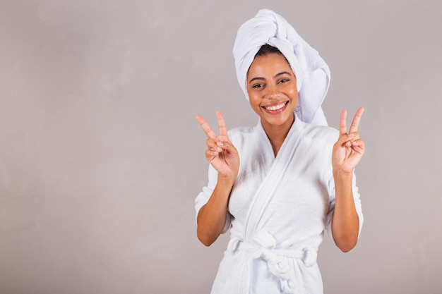 Mooie Braziliaanse zwarte vrouw die een badjas en een handdoek draagt, vrede en liefde voor goede vibes glimlacht