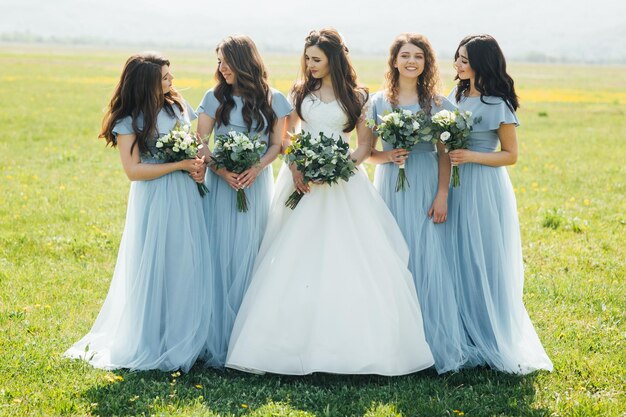 mooie bruid en haar bruidsmeisjes staan met bloemen in de natuur