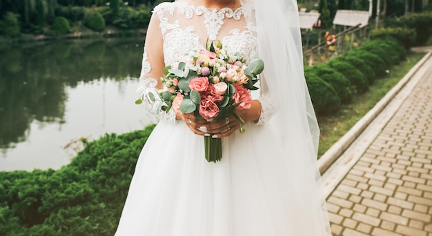 Mooie bruid houdt boeket in handen Trouwfoto buitenshuis Witte jurk met lange mouwen en wit kant