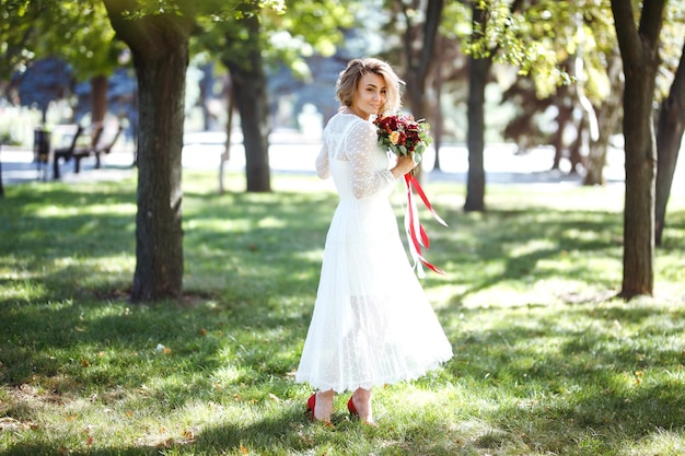 Mooie bruid met bruidsboeket in park Elegante vrouw met professionele make-up en kapsel