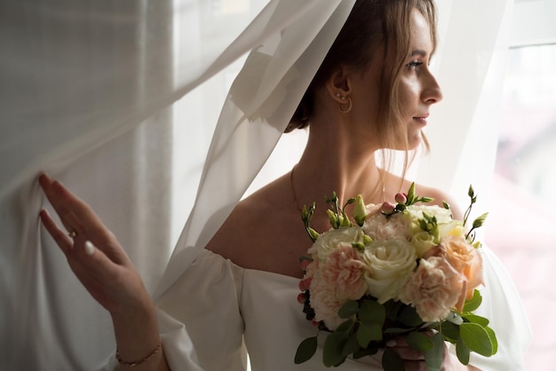 Mooie bruid met huwelijksboeket dichtbij venster
