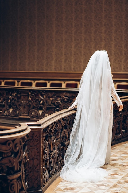 Mooie bruid met lange sluier in kanten gewaad bruids boudoir in ochtend achteraanzicht stijlvolle vrouw in oude kamer wandelen