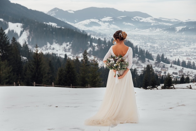 Mooie bruid poseert met een rijk bruidsboeket in de winterbergen
