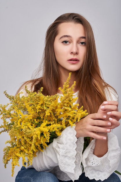 Mooie bruinharige vrouw met gele Mimosa bloemen op een witte achtergrond. Lente portret van een meisje