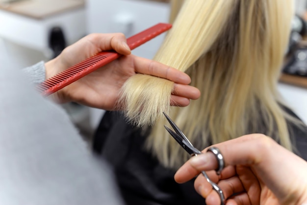 Mooie brunette die als kapper werkt, knipt de uiteinden van het haar van de klant in een schoonheidssalon