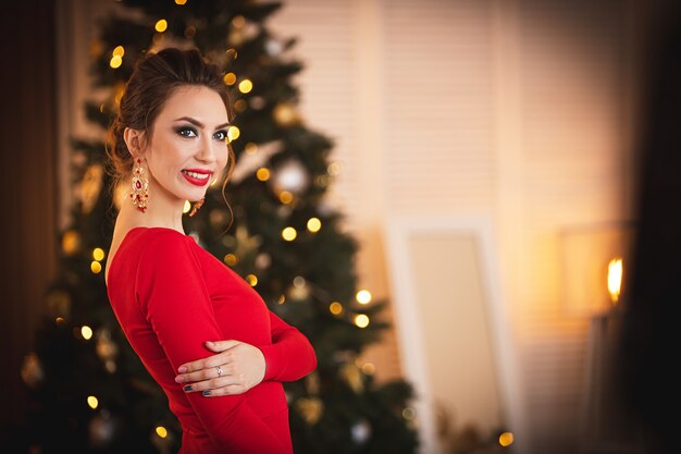 Mooie brunette in een rode jurk op de achtergrond van de kerstboom.