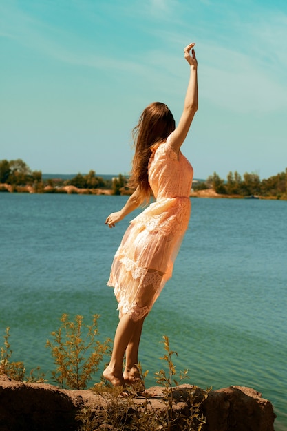 Mooie brunette in roze jurk op het strand wegkijkend